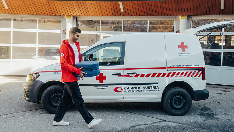 Mitarbeiter des Casino Seefeld trägt eine Box mit Essen zu einem Rot-Kreuz-Fahrzeug.   